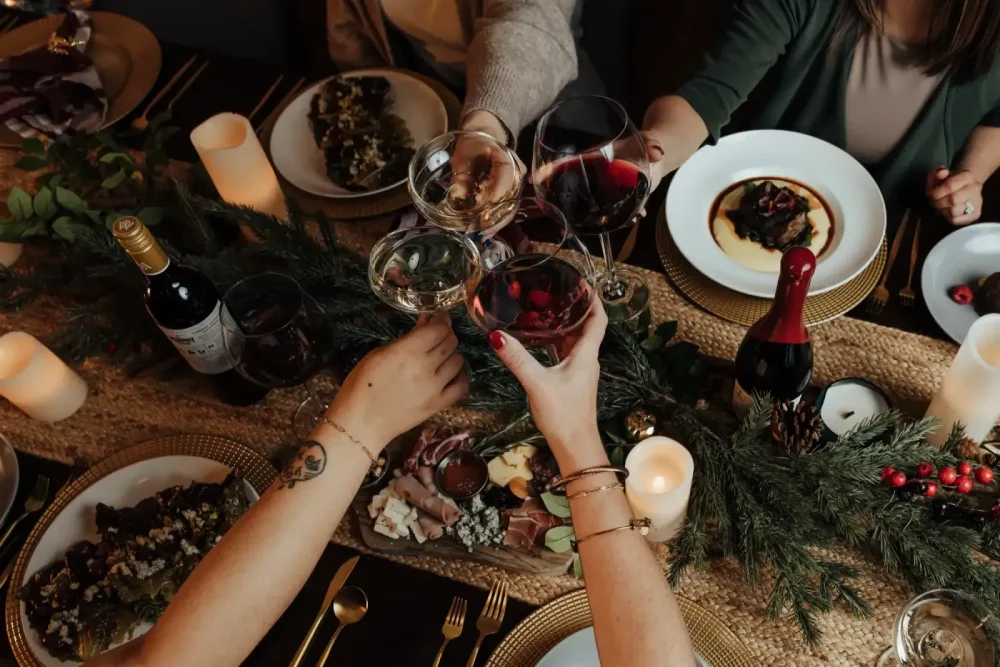 An overhead view of a group of people toasting with glasses of red, white, and rosé wine over an elegantly set dinner table.