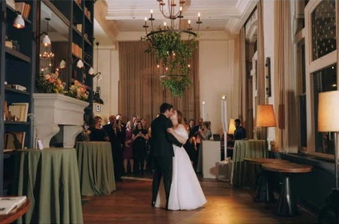 A bride and groom share a kiss while having their first dance in the middle of a grand, warmly lit reception hall.