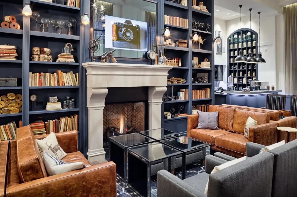 Cozy lounge with leather sofas, stone fireplace, and shelves filled with books and vintage items, creating a warm, inviting atmosphere.