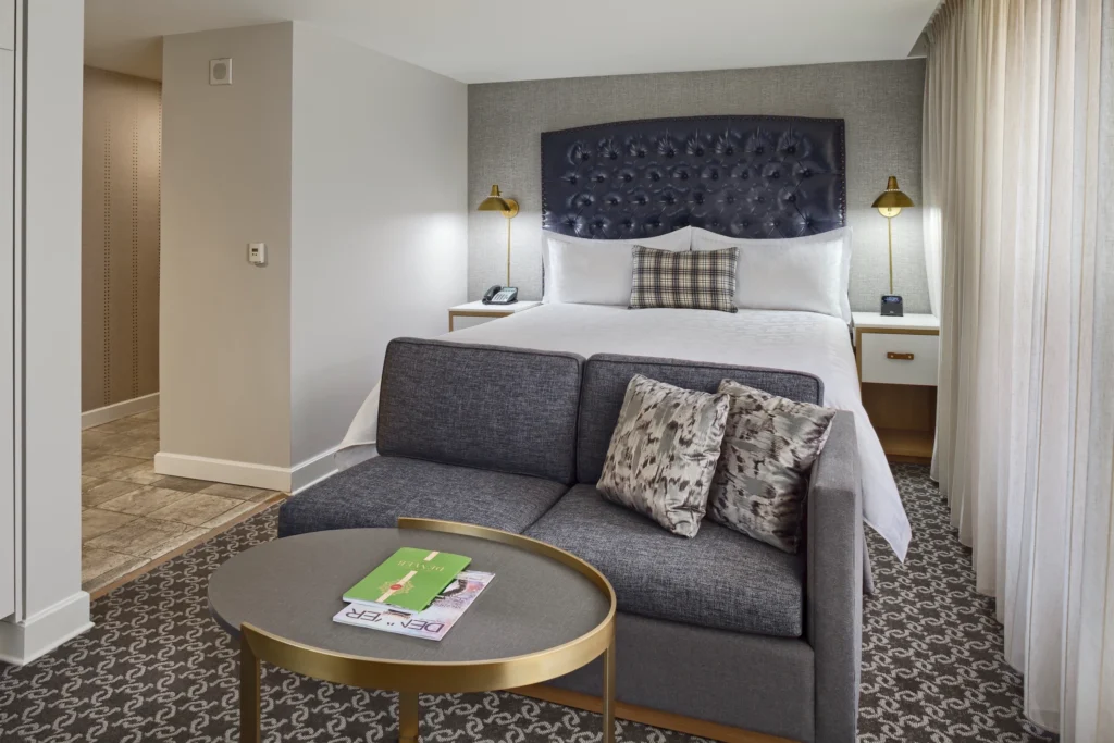 A modern hotel room featuring a plush bed with a tufted headboard, stylish seating area, and elegant decor.