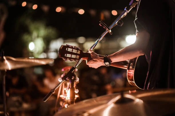A close-up of a musician's hands playing an acoustic guitar on a dimly lit stage during a live performance.